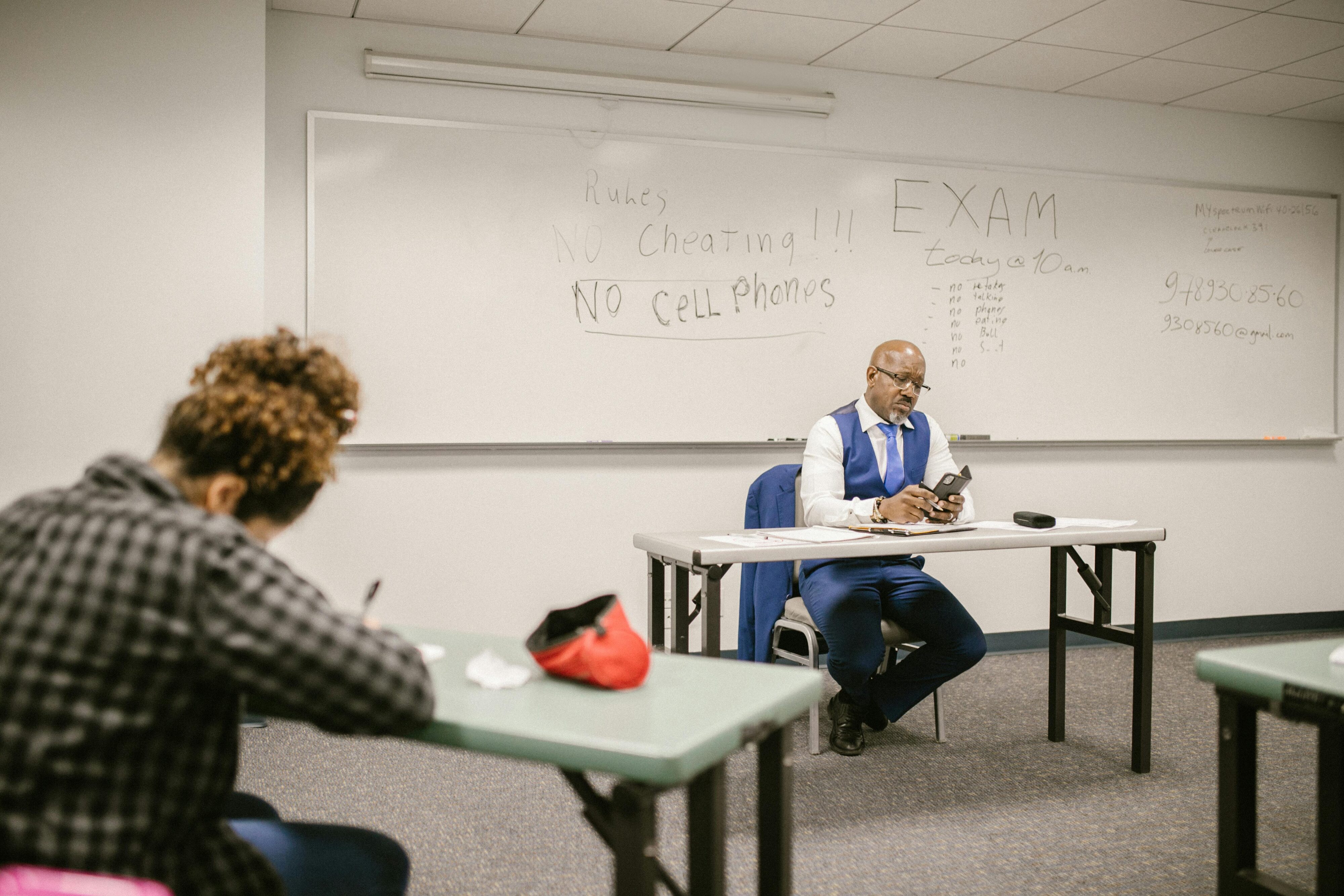 A proctor monitors an exam in a classroom setting with students taking tests.